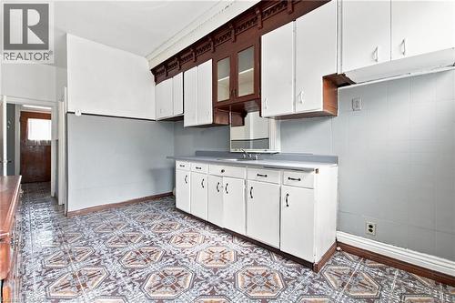 Kitchen featuring patterned floor tile, white base cabinetry with dark pulls, white upper cabinetry, and a dark wood-finish built-in with glass-front display cabinets - 128 Hess Street N, Hamilton, ON - Indoor Photo Showing Other Room