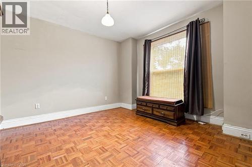Parquet wood flooring, a single pendant light fixture, and a large window with roller shades - 128 Hess Street N, Hamilton, ON - Indoor Photo Showing Other Room