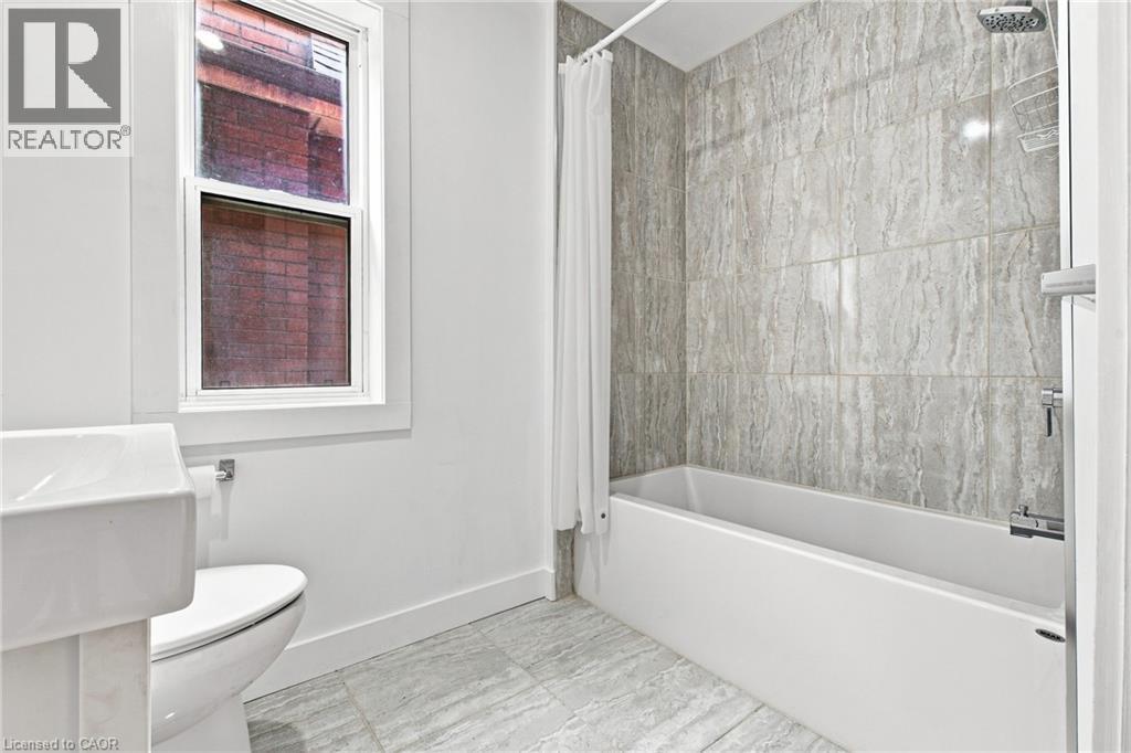 Bathtub with full-height tile surround, wall-mounted showerhead, and coordinating tile flooring - 128 Hess Street N, Hamilton, ON - Indoor Photo Showing Bathroom