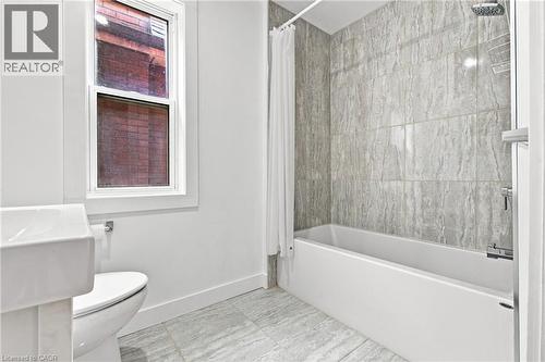 Bathtub with full-height tile surround, wall-mounted showerhead, and coordinating tile flooring - 128 Hess Street N, Hamilton, ON - Indoor Photo Showing Bathroom