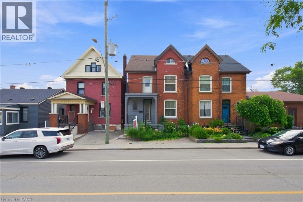 Brick exterior with contrasting trim, front porch with columns, gabled roofline, and landscaped front garden - 128 Hess Street N, Hamilton, ON - Outdoor With Balcony With Facade