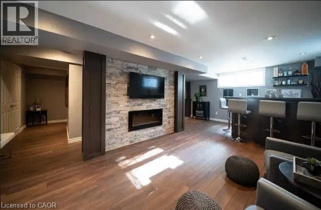 Finished basement featuring wood-finish flooring, recessed lighting, and a stone accent wall with a built-in electric fireplace - 4000 Medland Drive, Burlington, ON - Indoor Photo Showing Living Room With Fireplace
