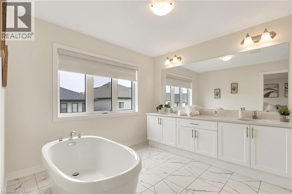 Freestanding soaking tub, dual vanity with undermount sinks, expansive mirror, white cabinetry, and large format floor tiling - 285 Broadacre Drive, Kitchener, ON - Indoor Photo Showing Bathroom