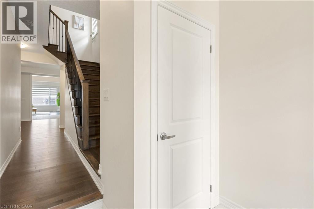 Wood-finish flooring throughout the hallway and staircase, dark wood staircase with wrought iron balusters, and a paneled interior door with a silver-finish handle - 285 Broadacre Drive, Kitchener, ON - Indoor Photo Showing Other Room