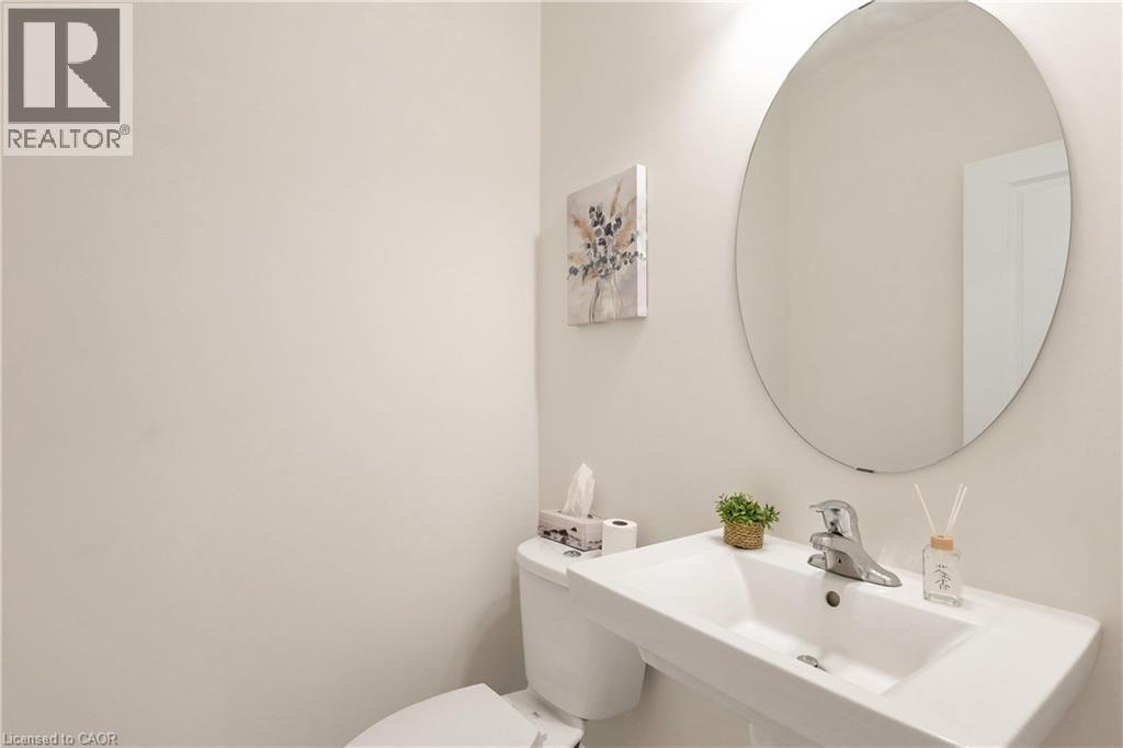 Wall-mounted rectangular sink with chrome faucet, circular mirror, and white toilet - 285 Broadacre Drive, Kitchener, ON - Indoor Photo Showing Bathroom