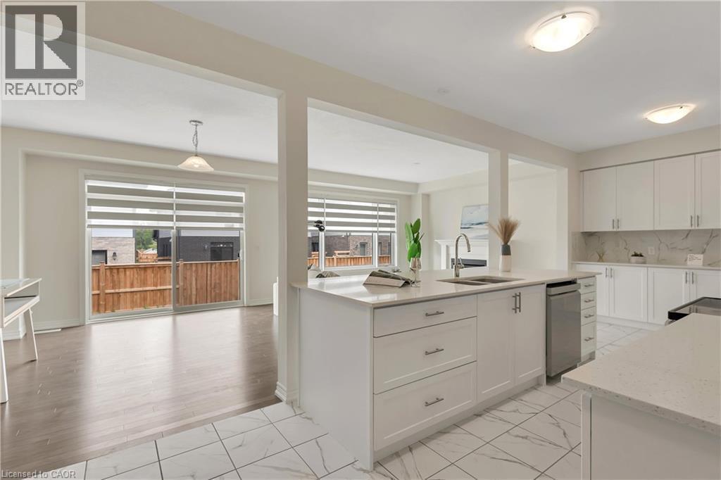 Open-concept design featuring a central kitchen island with an integrated sink, white cabinetry with silver hardware, white tile flooring, and wood-finish flooring in the adjoining space - 285 Broadacre Drive, Kitchener, ON - Indoor Photo Showing Kitchen With Double Sink