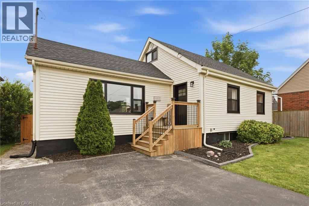 Cream-colored siding exterior with dark-framed windows, a dark shingle roof, a wooden deck, and a paved driveway - 481 Upper Gage Avenue, Hamilton, ON - Outdoor
