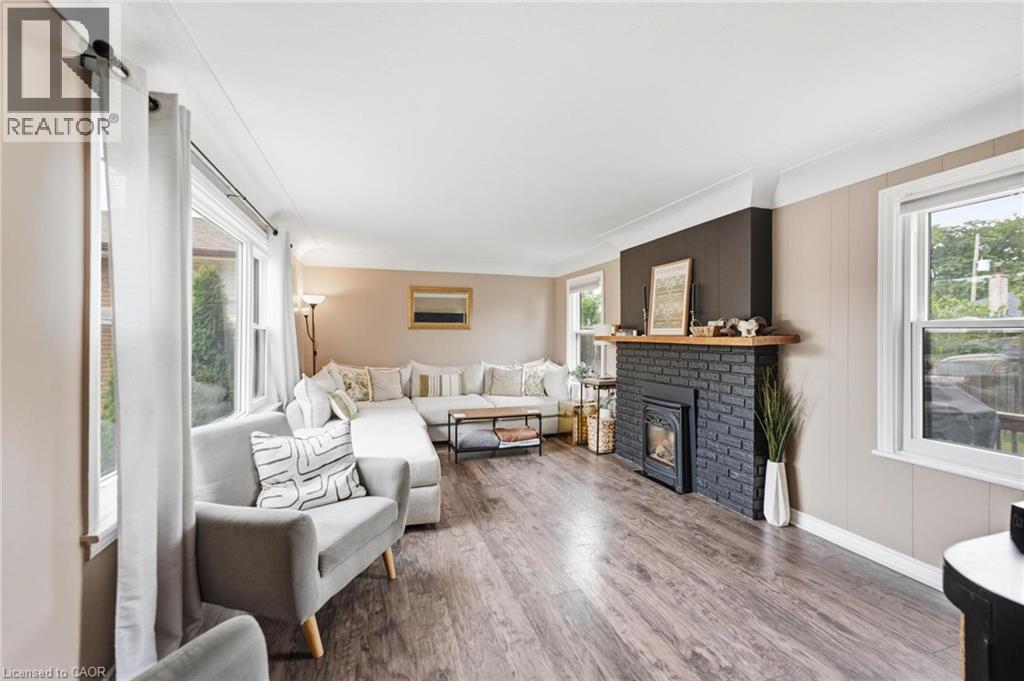 Spacious living area featuring wood-finish flooring, a black brick fireplace with a wood mantel, and multiple windows providing natural light - 481 Upper Gage Avenue, Hamilton, ON - Indoor Photo Showing Living Room With Fireplace