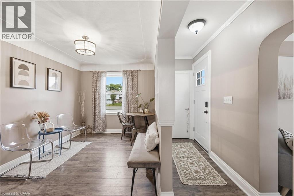 Inviting entryway featuring wood-finish flooring extending into the main living areas, a white entry door, and a decorative overhead light fixture - 481 Upper Gage Avenue, Hamilton, ON - Indoor