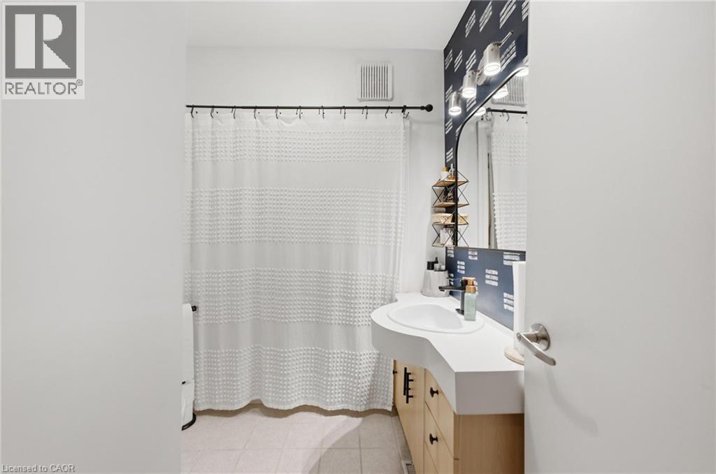 Bathroom featuring a vanity with an integrated sink, three-light fixture, and patterned accent wall - 481 Upper Gage Avenue, Hamilton, ON - Indoor Photo Showing Bathroom