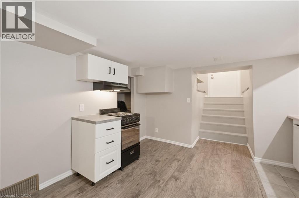 Basement kitchen area featuring a freestanding black and stainless steel range, range hood, white upper and lower cabinetry with dark hardware, a light-toned countertop, and private entrance - 481 Upper Gage Avenue, Hamilton, ON - Indoor Photo Showing Other Room