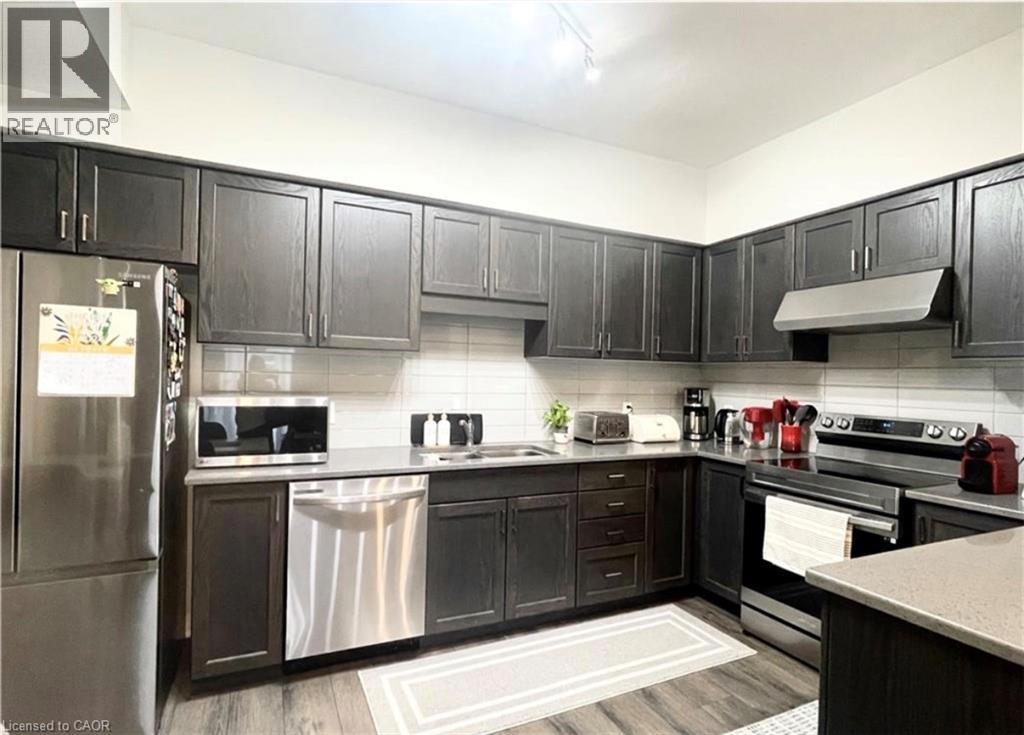 Kitchen featuring dark wood-finish cabinetry, stainless steel appliances, a white subway tile backsplash, light-toned countertops, and wood-finish flooring - 17 Visionary Avenue, Kitchener, ON - Indoor Photo Showing Kitchen With Double Sink With Upgraded Kitchen