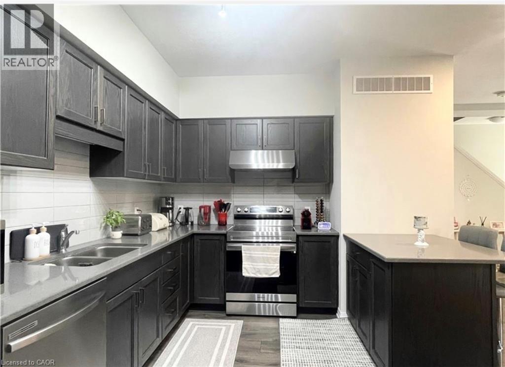 Kitchen featuring dark wood-finish cabinetry, light stone countertops, white subway tile backsplash, stainless steel appliances, and a built-in kitchen island - 17 Visionary Avenue, Kitchener, ON - Indoor Photo Showing Kitchen With Double Sink With Upgraded Kitchen