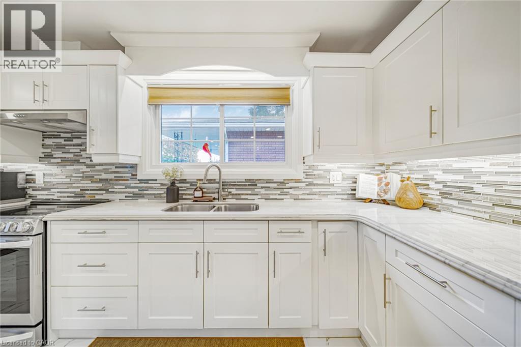 White shaker-style cabinetry, stainless steel sink, mixed-material backsplash, white countertops, and under-cabinet lighting - 24 Garvey Crescent, Hamilton, ON - Indoor Photo Showing Kitchen With Double Sink With Upgraded Kitchen