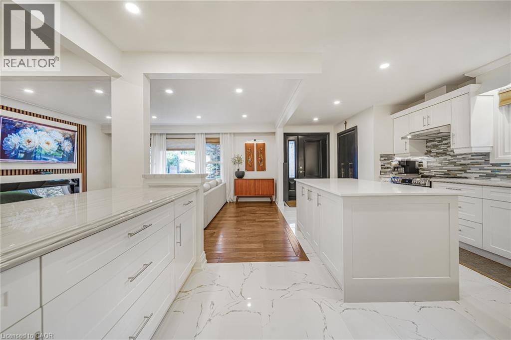 White cabinetry with brushed nickel hardware, expansive kitchen island, white countertops, tile backsplash, and recessed lighting - 24 Garvey Crescent, Hamilton, ON - Indoor Photo Showing Kitchen With Upgraded Kitchen