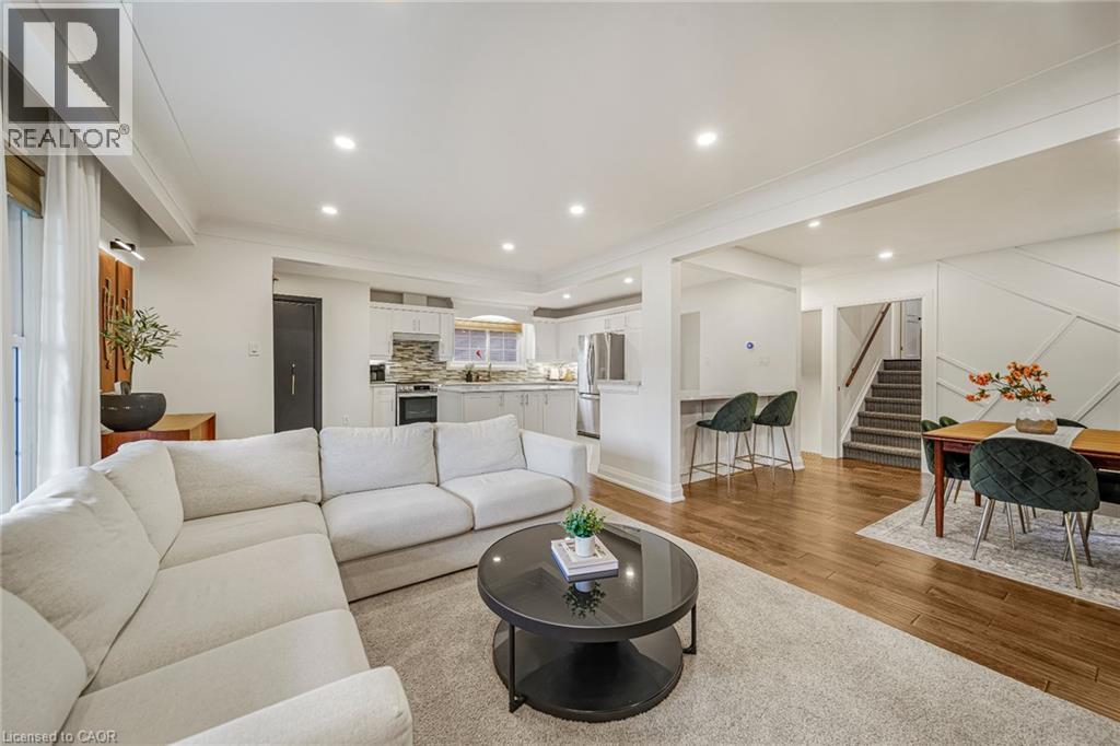 Open-concept living area featuring wood-finish flooring, recessed lighting, a kitchen pass-through, a staircase with carpeted treads, and a decorative accent wall - 24 Garvey Crescent, Hamilton, ON - Indoor Photo Showing Living Room