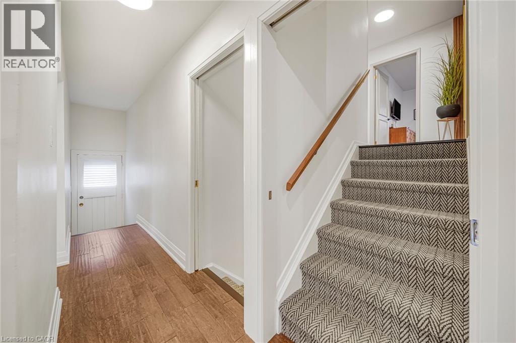 Wood-finish flooring, white paneled door with louvered window, recessed lighting, carpeted stairs with geometric pattern, and a natural wood handrail - 24 Garvey Crescent, Hamilton, ON - Indoor Photo Showing Other Room