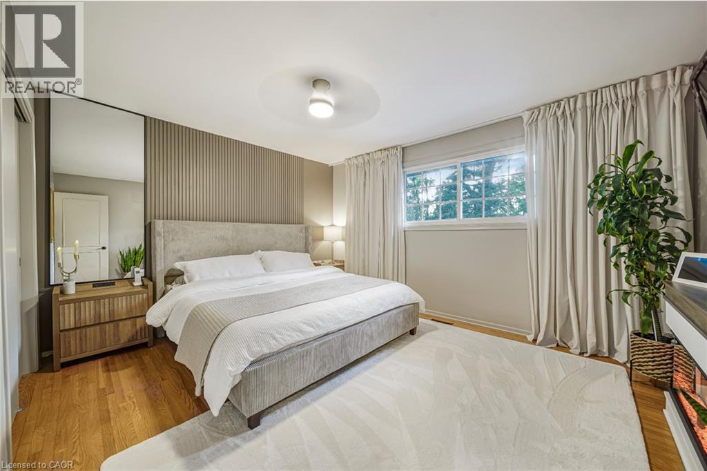 Wood-finish flooring with a light area rug, featuring a window with white trim, and a textured accent wall - 24 Garvey Crescent, Hamilton, ON - Indoor Photo Showing Bedroom