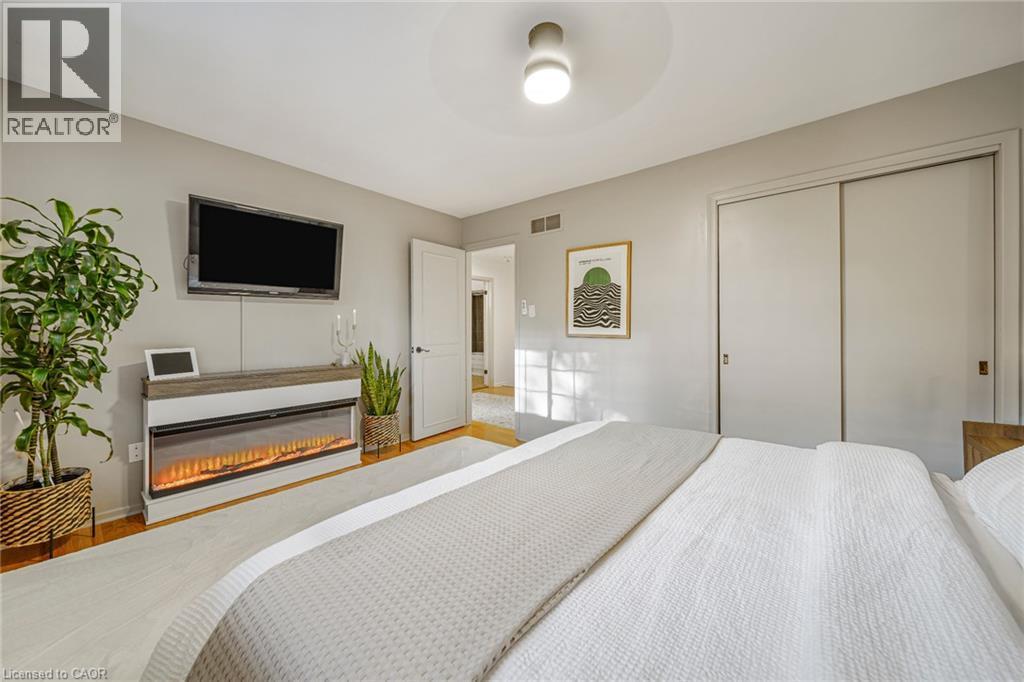 Hardwood-style flooring, contemporary ceiling light fixture, white interior door, sliding closet doors, and a linear electric fireplace - 24 Garvey Crescent, Hamilton, ON - Indoor Photo Showing Bedroom