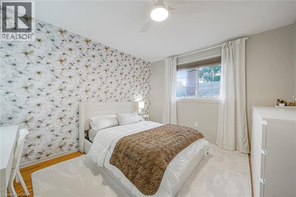 Floral pattern accent wall, neutral wall paint, wood-finish flooring, ceiling fan with integrated lighting, and a window with blinds - 24 Garvey Crescent, Hamilton, ON - Indoor Photo Showing Bedroom