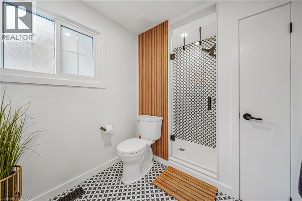White framed window, patterned floor tile, slatted wood-finish accent wall, glass enclosed shower, and black hardware - 24 Garvey Crescent, Hamilton, ON - Indoor Photo Showing Other Room
