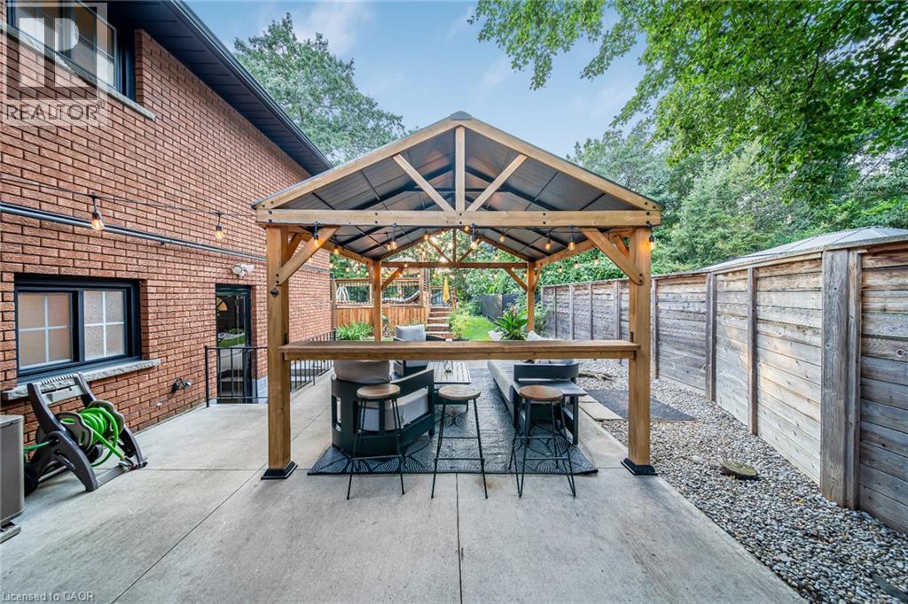 Concrete patio with a wooden gazebo, privacy fence, and brick exterior - 24 Garvey Crescent, Hamilton, ON - Outdoor With Exterior