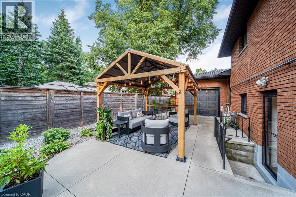 Wood pergola with built-in lighting, concrete patio, brick exterior, attached garage, and privacy fencing - 24 Garvey Crescent, Hamilton, ON - Outdoor With Deck Patio Veranda