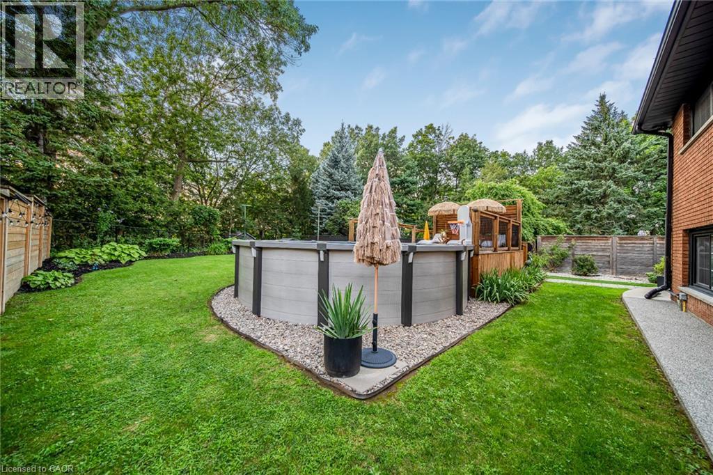 Expansive backyard featuring a manicured lawn, an above-ground pool with surrounding gravel, and a wooden deck structure - 24 Garvey Crescent, Hamilton, ON - Outdoor