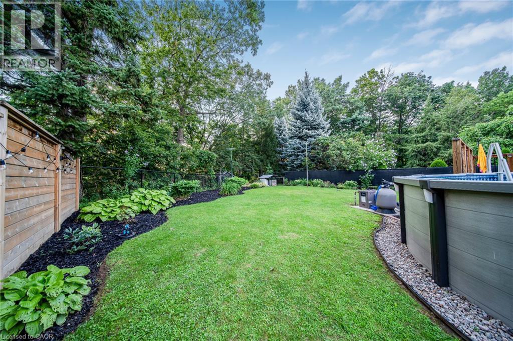 Manicured lawn, mature trees, wood-slat fence, above-ground pool, and landscaped garden beds - 24 Garvey Crescent, Hamilton, ON - Outdoor