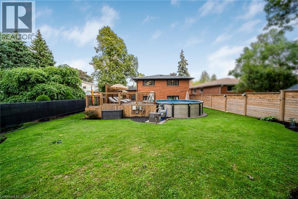 Expansive green lawn with a wood deck, above-ground pool, and wood fencing - 24 Garvey Crescent, Hamilton, ON - Outdoor With Backyard
