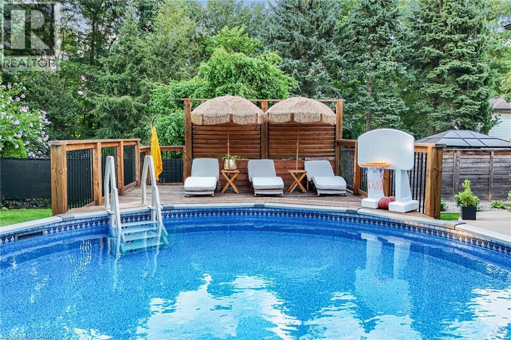 Expansive pool with patterned lining, surrounded by a wood-plank deck with railing, and privacy screen - 24 Garvey Crescent, Hamilton, ON - Outdoor With In Ground Pool With Deck Patio Veranda