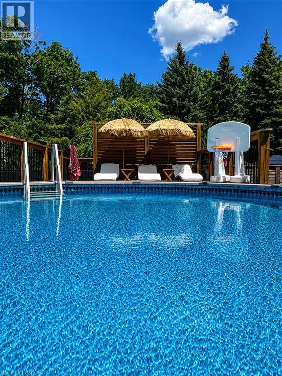 In-ground pool featuring a bright blue liner, perimeter fencing, and surrounding mature trees - 24 Garvey Crescent, Hamilton, ON - Outdoor With Above Ground Pool