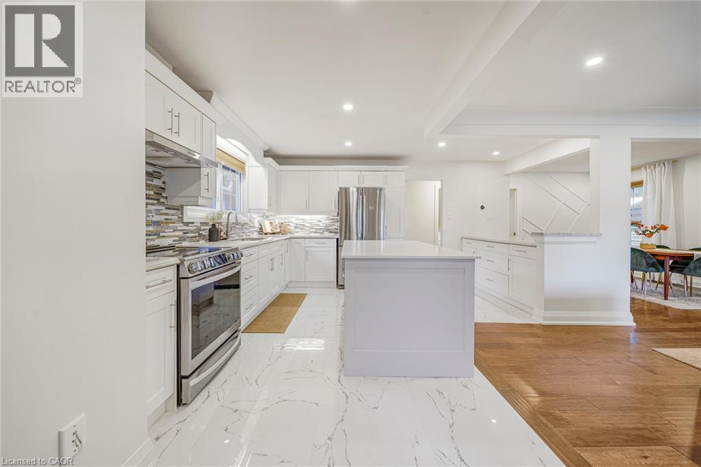 Contemporary kitchen featuring white cabinetry, a central island, stainless steel appliances, and a tiled backsplash - 24 Garvey Crescent, Hamilton, ON - Indoor Photo Showing Kitchen With Upgraded Kitchen