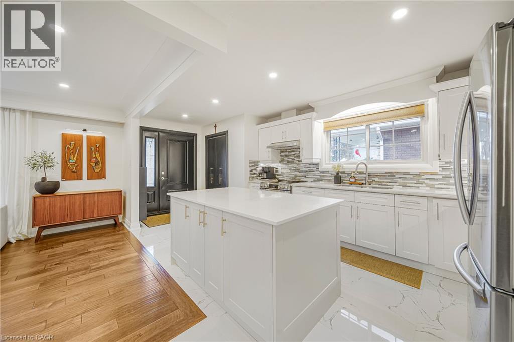 Modern kitchen with a central island, white cabinetry, integrated stainless steel appliances, and a tiled backsplash - 24 Garvey Crescent, Hamilton, ON - Indoor Photo Showing Kitchen With Upgraded Kitchen