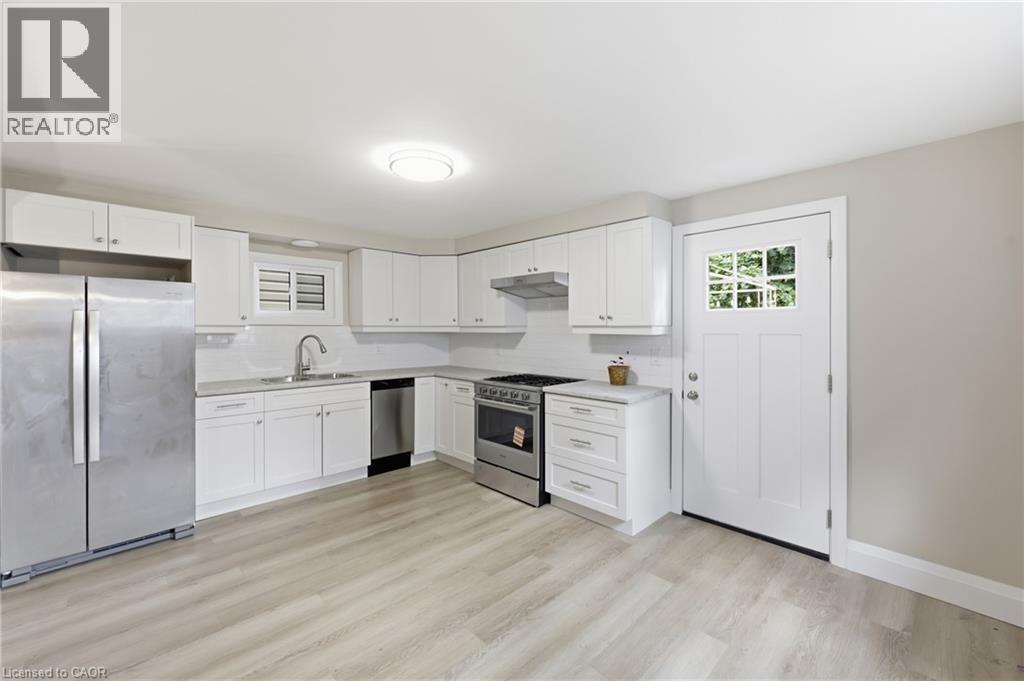White cabinetry, stainless steel appliances, light wood-finish flooring, white subway tile backsplash, and a paneled entry door with divided lites - 56 Harmony Avenue, Hamilton, ON - Indoor Photo Showing Kitchen