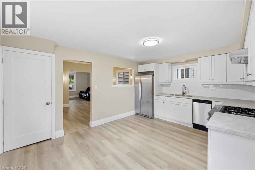 Kitchen with wood-finish flooring, white cabinetry, stainless steel appliances, and a tiled backsplash - 56 Harmony Avenue, Hamilton, ON - Indoor Photo Showing Kitchen