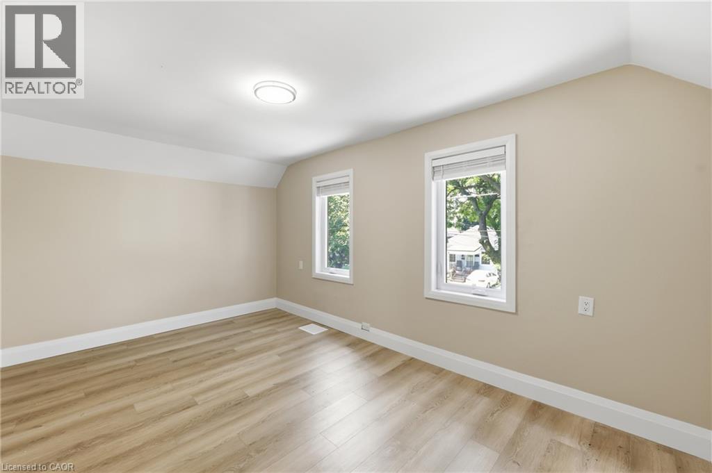Neutral wall tones, wood-finish flooring, two windows with white blinds, and a flush-mount ceiling light - 56 Harmony Avenue, Hamilton, ON - Indoor Photo Showing Other Room