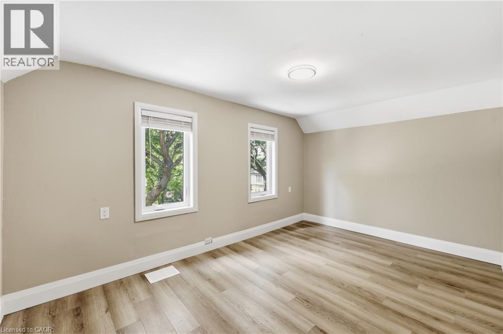 Wood-finish flooring with white trim, neutral wall color, two windows, and a flush-mount ceiling light - 56 Harmony Avenue, Hamilton, ON - Indoor Photo Showing Other Room