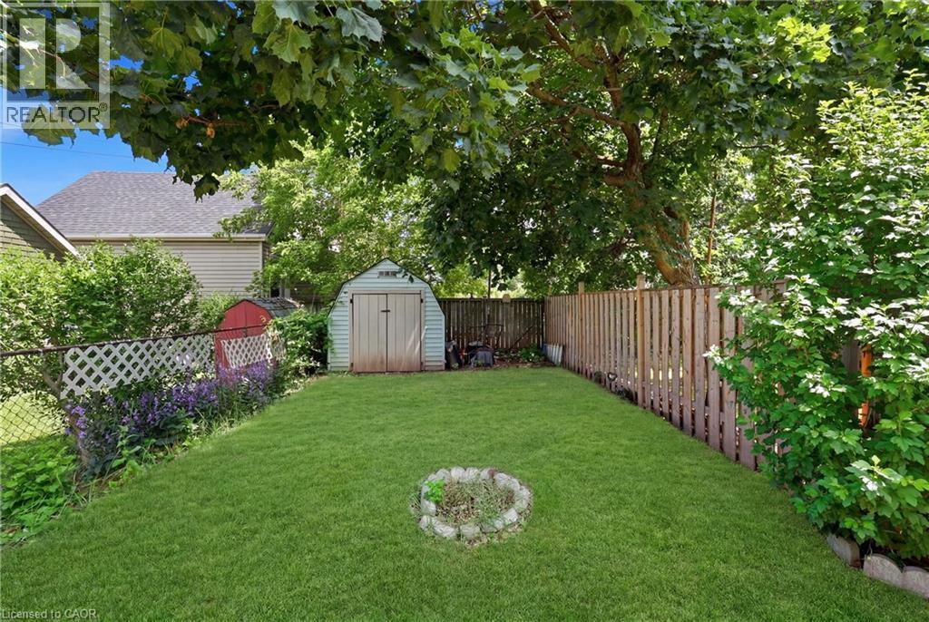 Expansive backyard featuring a lush, manicured lawn anchored by mature shade trees, wooden privacy fencing, a storage shed, and a fire pit ring—ideal for outdoor entertaining and recreation - 56 Harmony Avenue, Hamilton, ON - Outdoor