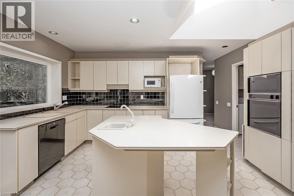 Kitchen featuring hexagonal tile flooring, light-toned cabinetry, a skylight, a large window, and integrated double ovens - 4189 Inglewood Drive, Burlington, ON - Indoor Photo Showing Kitchen With Double Sink