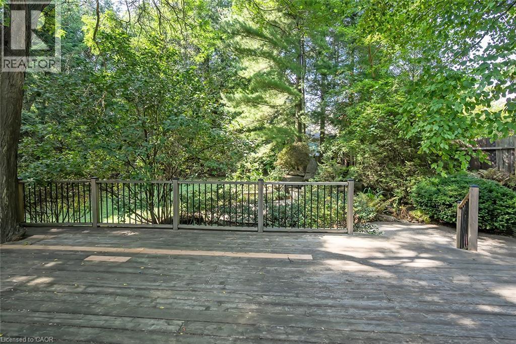 Expansive wood deck with a dark wood railing, surrounded by mature trees and lush landscaping - 4189 Inglewood Drive, Burlington, ON - Outdoor