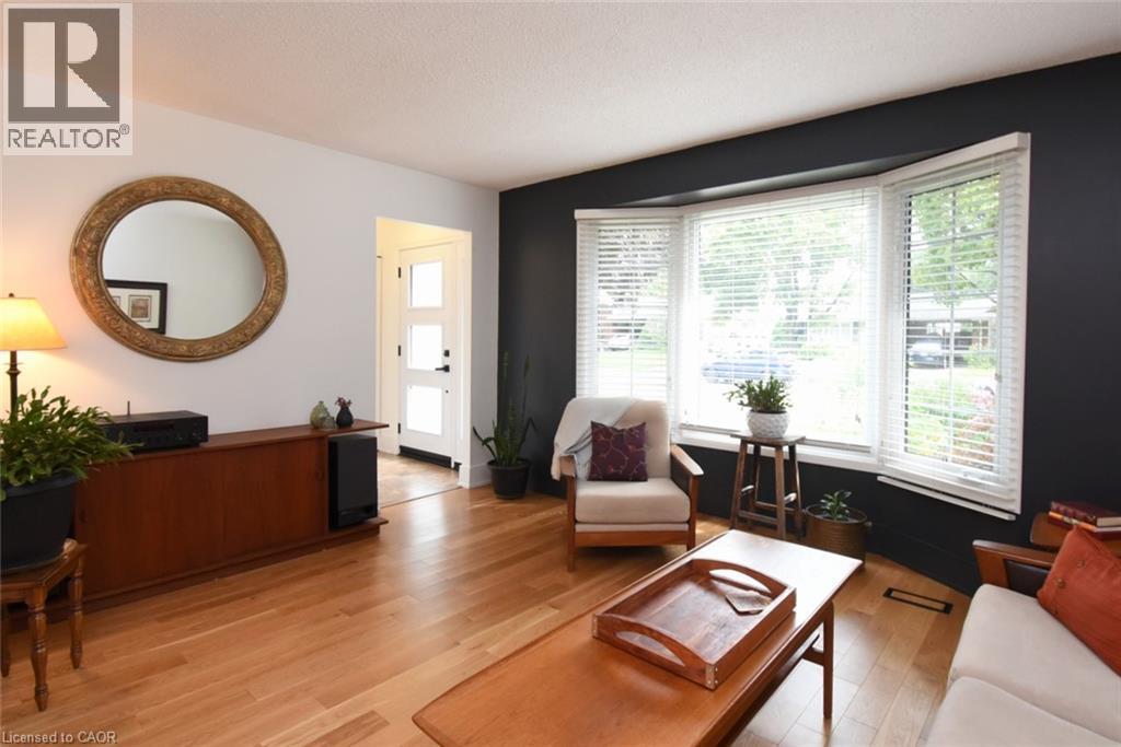 Hardwood flooring, bay windows with blinds, white entry door with frosted glass panels, and a built-in wood-finish credenza - 374 Brigadoon Drive, Hamilton, ON - Indoor Photo Showing Living Room