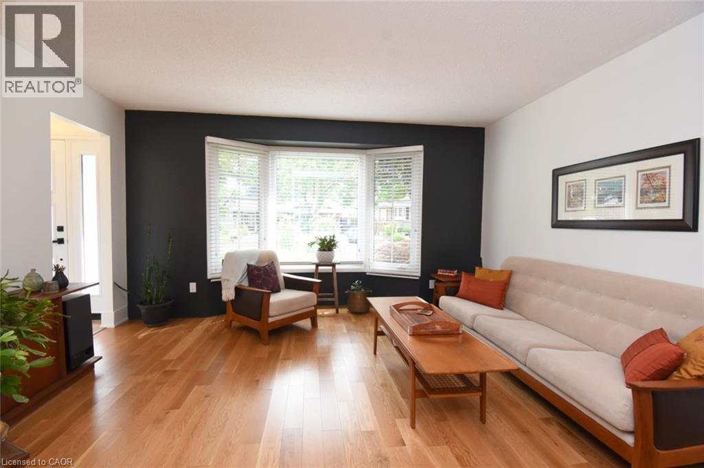 Hardwood flooring, bay window, white window blinds, dark accent wall, white walls - 374 Brigadoon Drive, Hamilton, ON - Indoor Photo Showing Living Room