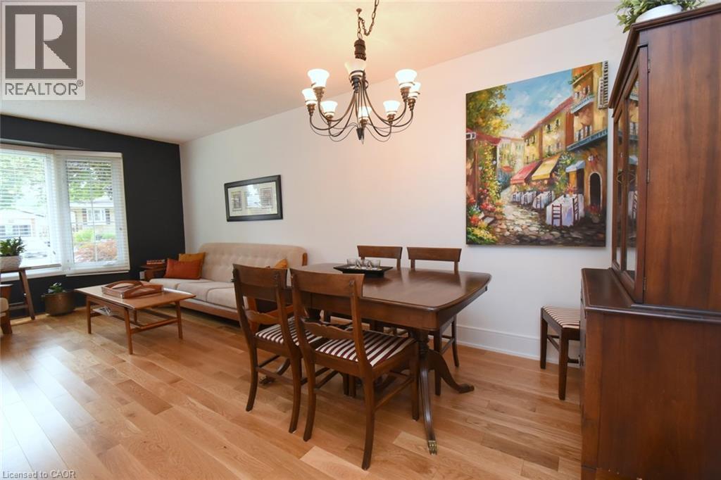 Hardwood flooring, bay window with blinds, modern chandelier, dark accent wall, and built-in wood cabinetry - 374 Brigadoon Drive, Hamilton, ON - Indoor Photo Showing Dining Room