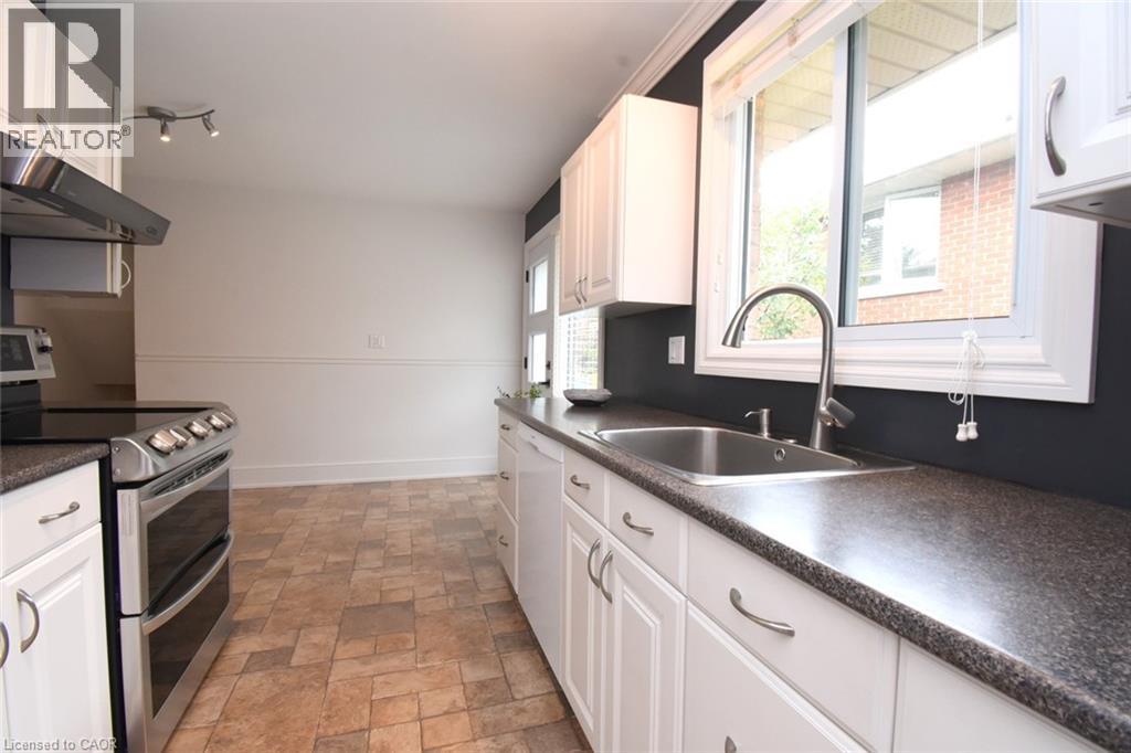 White cabinetry, stainless steel appliances, stainless steel sink with gooseneck faucet, dark countertops, and patterned floor tiles - 374 Brigadoon Drive, Hamilton, ON - Indoor Photo Showing Kitchen