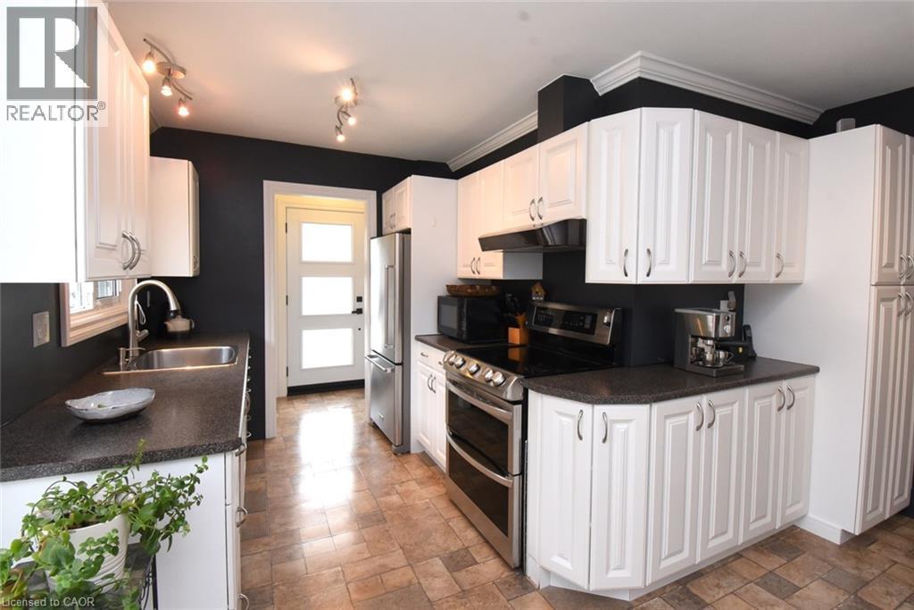 White cabinetry with curved silver-tone hardware, dark countertops, stainless steel appliances, track lighting, and a modern white door with frosted glass panels - 374 Brigadoon Drive, Hamilton, ON - Indoor Photo Showing Kitchen