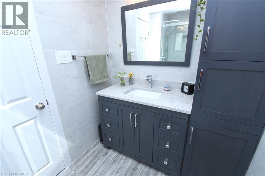 White paneled door opening to a bathroom featuring a vanity with a white rectangular sink, light-colored countertop, and dark cabinetry - 374 Brigadoon Drive, Hamilton, ON - Indoor Photo Showing Bathroom