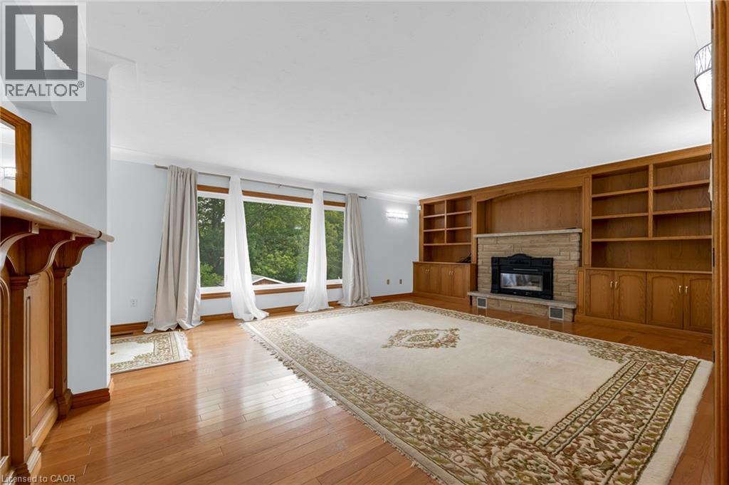 Wood-finish flooring throughout, featuring a stone fireplace with a built-in wood surround, extensive built-in shelving, and large windows - 35 Glen Park Court, Hamilton, ON - Indoor Photo Showing Other Room With Fireplace