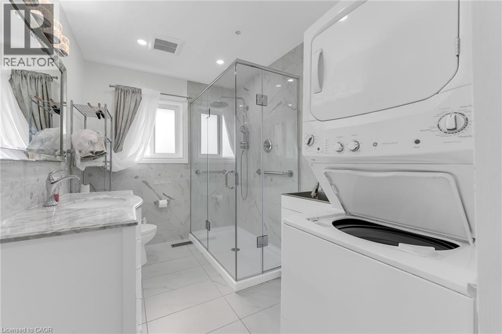 Contemporary bathroom featuring a glass-enclosed shower, built-in vanity with a stone countertop, and a stacked washer and dryer - 35 Glen Park Court, Hamilton, ON - Indoor Photo Showing Laundry Room