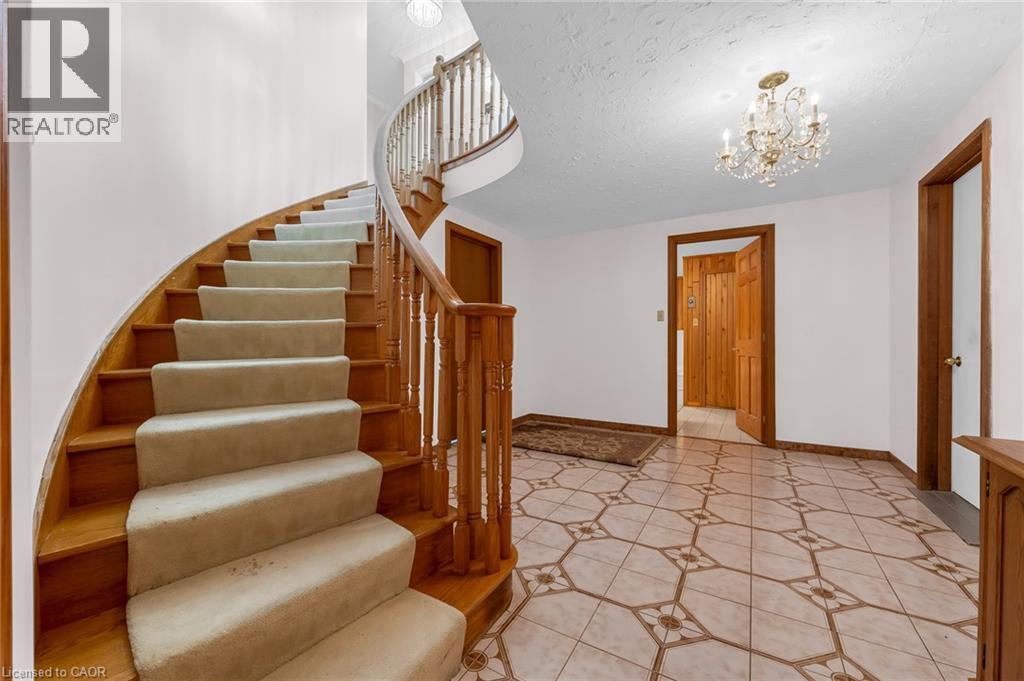 Curved staircase with wood treads and carpet runners, detailed wood banister, chandelier lighting, and patterned tile flooring - 35 Glen Park Court, Hamilton, ON - Indoor Photo Showing Other Room